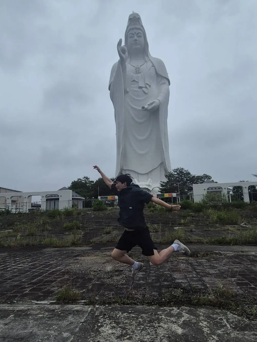 거대한 흰색 관음상 앞에서 두 팔을 벌리고 뛰어오른 모습.